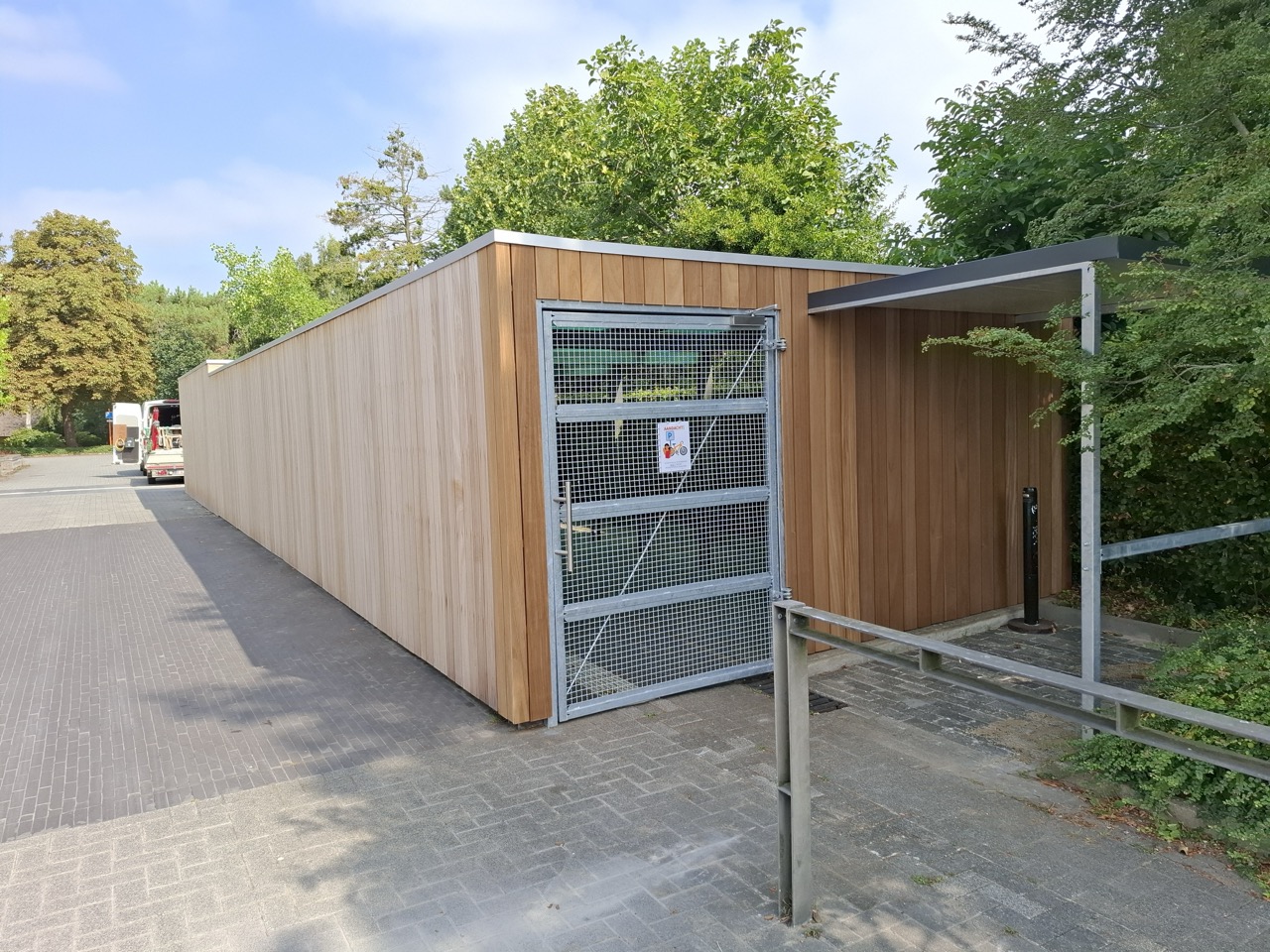 moderne houten afvalschuif met metalen toegangspoort en overkapping in groene buitenomgeving