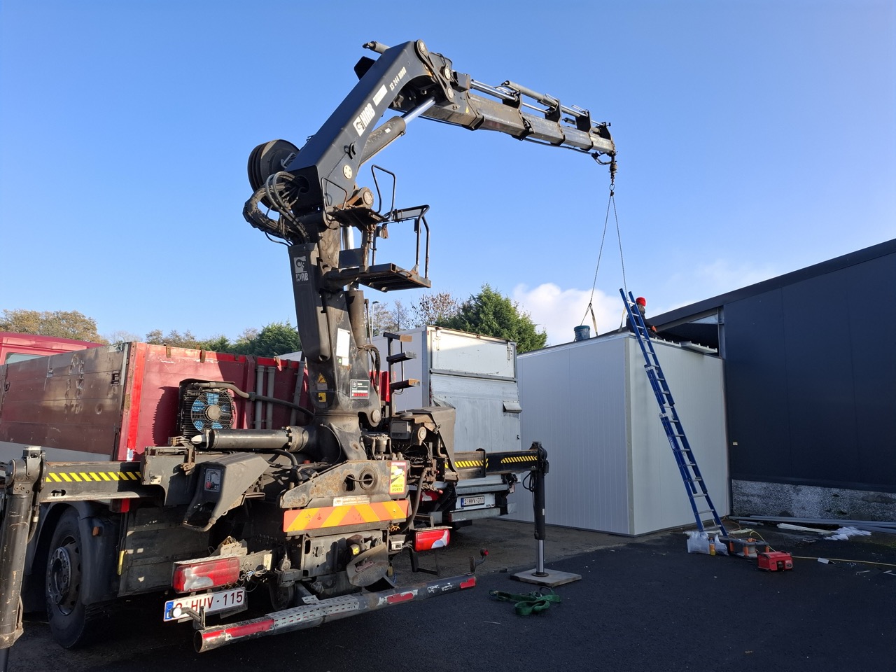 Mobiele kraan op vrachtwagen tilt prefab container op bouwterrein met werknemer op ladder