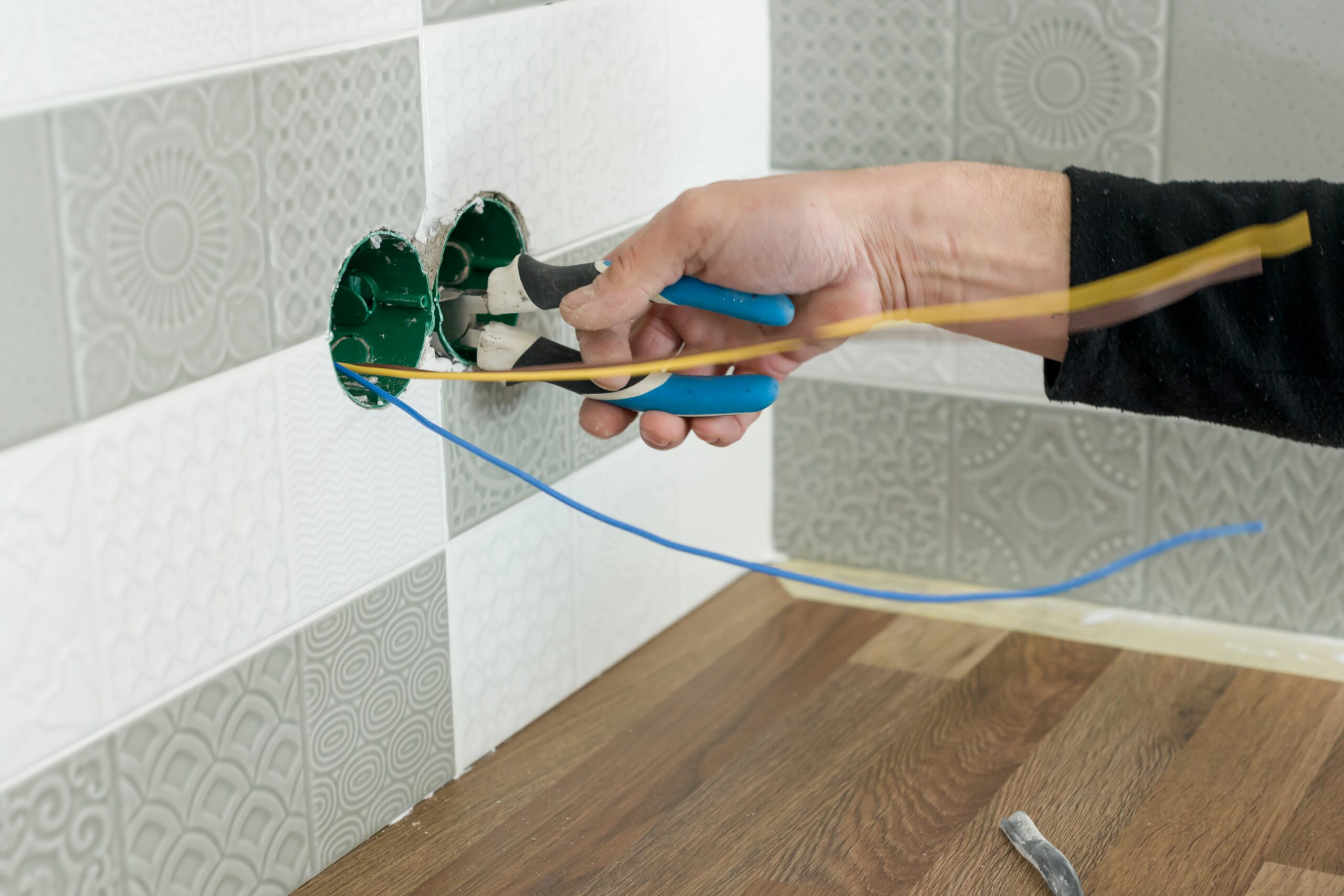 Elektricien werkt aan bedrading in ingegraven wanddoos met blauwe en gele kabels