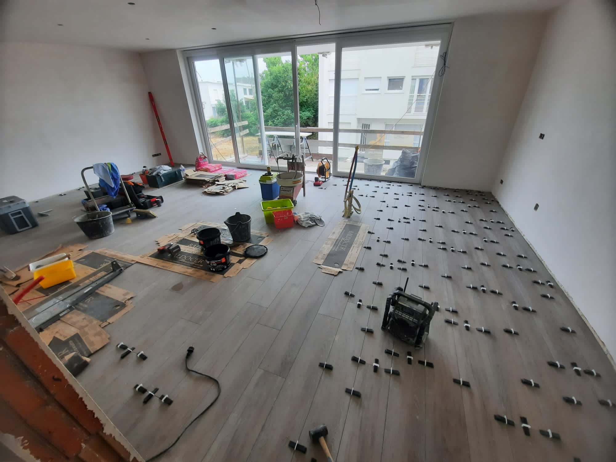 vloerenleggen in woonkamer met grote schuiframen en gereedschap verspreid over de vloer